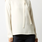 A woman wears the Ann Mashburn Pippa Top, a luxe crepe de chine tie-neck blouse with long sleeves, paired with dark pants and standing against a plain background.