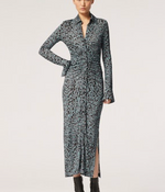 A woman wears the Altuzarra Claudia Dress, a long-sleeve, ankle-length style in blue and black abstract print with ruched detail, paired with black ankle boots, standing against a plain background.