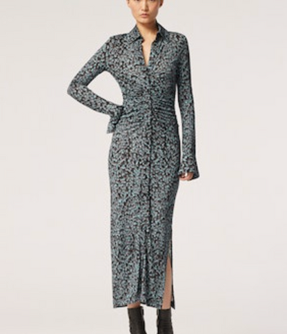 A woman wears the Altuzarra Claudia Dress, a long-sleeve, ankle-length style in blue and black abstract print with ruched detail, paired with black ankle boots, standing against a plain background.