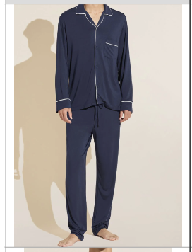 A person stands barefoot wearing the Eberjey Willam Long PJ Set—navy blue men’s pajamas crafted from temperature-regulating TENCEL™ Modal, featuring a coordinating long-sleeve button-up top with white piping.