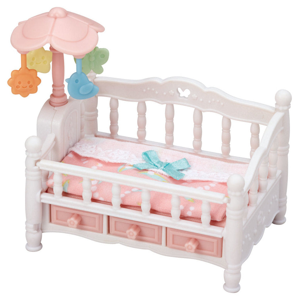 The Calico Critters Crib with Mobile is a small white and pink toy crib featuring a pink mattress, blue bow, three bottom drawers, and a pastel mobile attached to one corner—ideal as dollhouse furniture or as part of a baby nursery set.