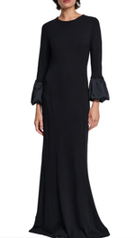 A woman stands against a white background wearing the Dorothee Schumacher Cloudy Allure Dress—a black, wrinkle-free travel jersey midi dress with long sleeves and satin bubble cuffs.