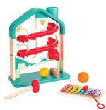 The Melody Mansion Ball Run by Hape is a house-shaped wooden toy set that features a ball rolling game with a red mallet, yellow and orange balls, and a small rainbow-colored xylophone board complete with a red stick.
