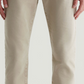 A person wearing light beige Tellis Selvage jeans by AG Jeans, featuring rolled cuffs and crafted from Japanese stretch selvage denim, shown waist to ankle against a plain background.