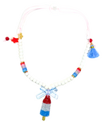 Add a playful touch to any outfit with the Lillies & Roses Popsicle Rocket Red White Blue Necklace, featuring white beads, red and blue accents, a blue tassel, bow, star charm, and a glittery rocket popsicle pendant.