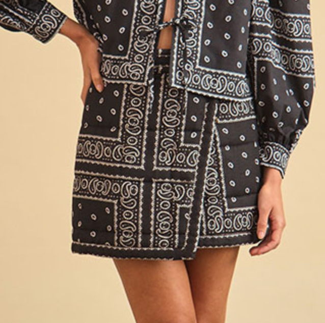 Wearing the Hunter Bell NYC Powell Skirt and a matching black and white paisley long-sleeve top, a person stands confidently with one hand on their hip.