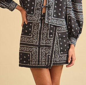 Wearing the Hunter Bell NYC Powell Skirt and a matching black and white paisley long-sleeve top, a person stands confidently with one hand on their hip.