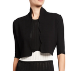 A woman wears the Lela Rose Scallop Trim Knit Bolero over a black and white knit dress with vertical perforated patterns.