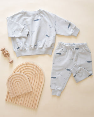 A light grey Quincy Mae Baby Boys' and Boys' Relaxed Fleece Sweatshirt set with whale prints, shown with wooden stacking arches and a rattle on a cream background—a cozy must-have for your toddler.