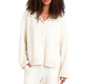 A woman wears the Sablyn Lilou Cashmere Jacket, a loose-fitting, cream-colored button-up, paired with matching pants. Her hand is in her pocket and her face is partially out of frame.