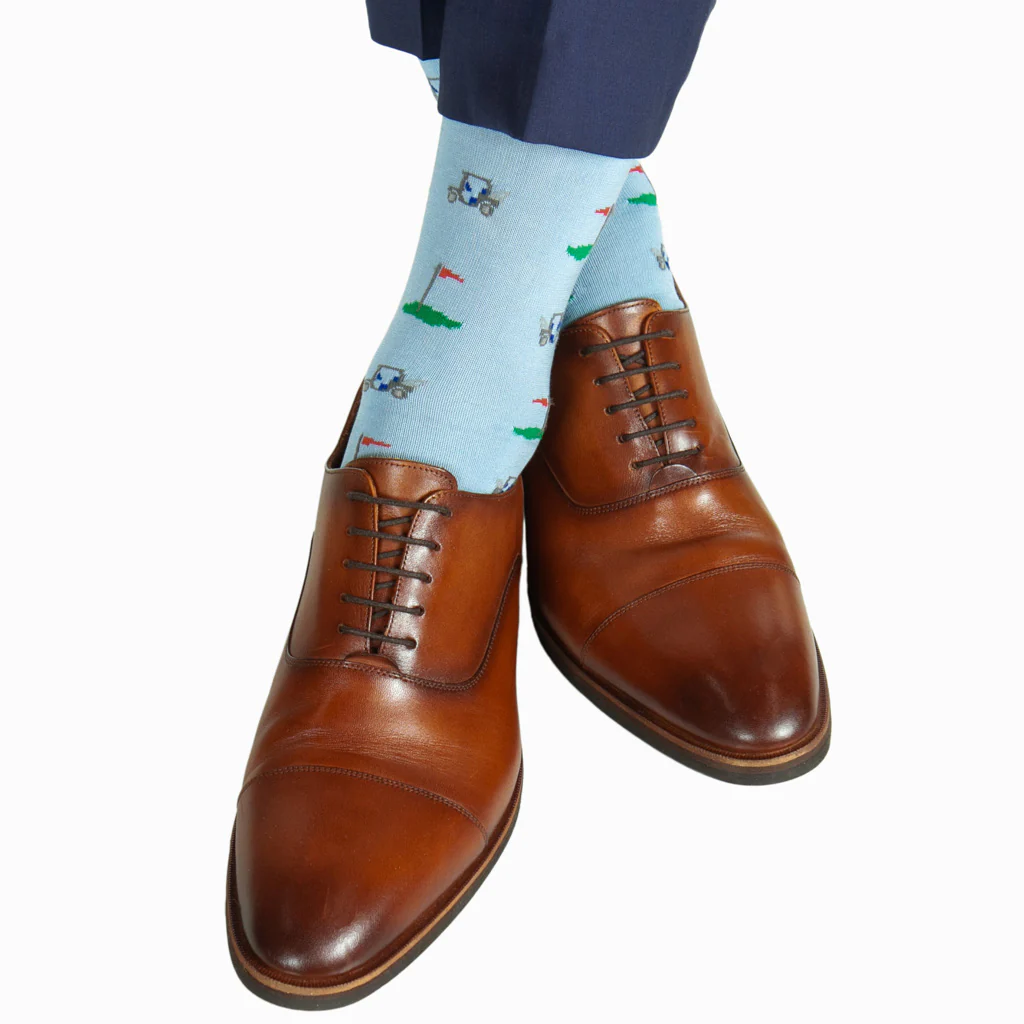 A man wearing Dapper Classics Golf Cart Cotton Mid-Calf Socks, featuring a golf course and cart motif, pairs them with brown leather dress shoes. These stylish socks add comfort and flair to any outfit.
