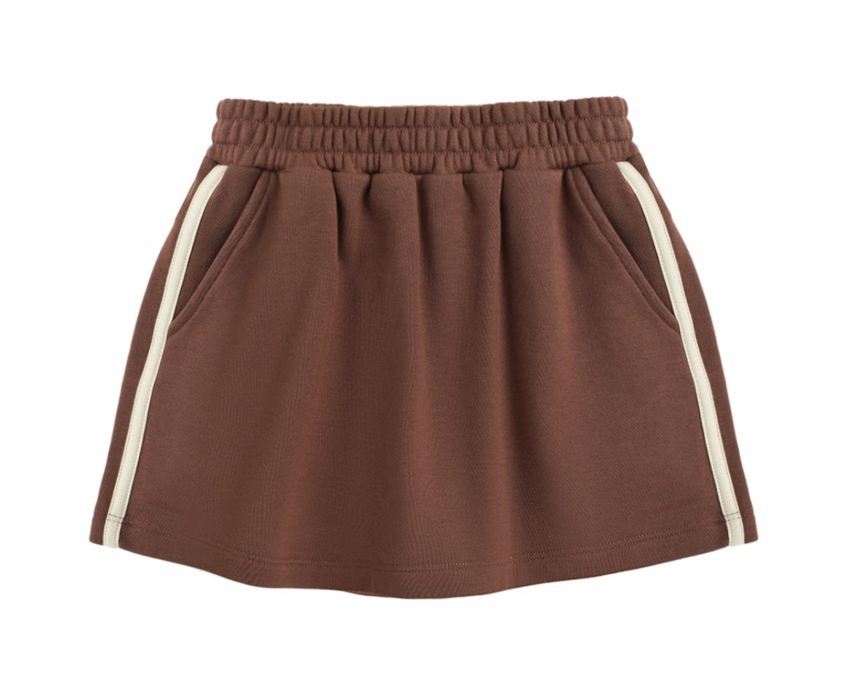 The Girls’ Sports Skirt by Rylee & Cru, featuring an elastic waistband, side pockets, and white vertical stripes along the sides, is laid flat on a white background.
