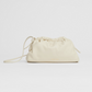 The Mansur Gavriel Mini Cloud Clutch is a small, handcrafted Italian drawstring pouch in cream lamb leather, featuring a versatile strap. Its minimalist design stands out against a white background.