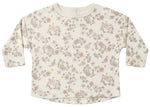 The Quincy Mae Baby and Kids’ Long Sleeve Tee features a round neckline, convenient shoulder snaps, and is crafted from soft organic brushed cotton with a delicate neutral-toned floral pattern on a cream background.