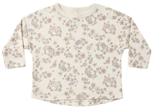 The Quincy Mae Baby and Kids’ Long Sleeve Tee features a round neckline, convenient shoulder snaps, and is crafted from soft organic brushed cotton with a delicate neutral-toned floral pattern on a cream background.