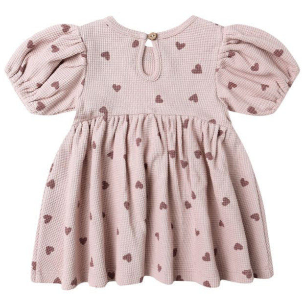 The Quincy Mae Baby Girls' and Girls' Darla Dress is a light pink babydoll with puffed short sleeves, a gathered skirt, brown heart prints, and a back button closure.