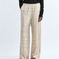 A person wearing Toteme’s Monogram Silk PJ Bottoms, featuring a subtle monogram pattern, styled with a black long-sleeve top and black sandals, stands against a plain background.