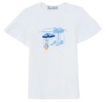 The Tartine et Chocolat Girls’ Beach Illustration T-Shirt is made from 100% cotton and showcases a delightful Santorini-inspired graphic in blue and orange, depicting a person lounging under a striped beach umbrella beside a chair, palm tree, and building. The design is completed with “Vanille et Chocolat” text above the illustration.