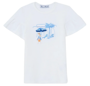 The Tartine et Chocolat Girls’ Beach Illustration T-Shirt is made from 100% cotton and showcases a delightful Santorini-inspired graphic in blue and orange, depicting a person lounging under a striped beach umbrella beside a chair, palm tree, and building. The design is completed with “Vanille et Chocolat” text above the illustration.