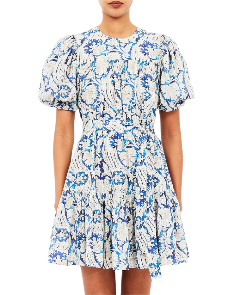 A woman wears the Ulla Johnson Rosalie Mini Dress, a short, puff-sleeve style with a blue and white floral print inspired by graphic botanicals and a fitted waist.
